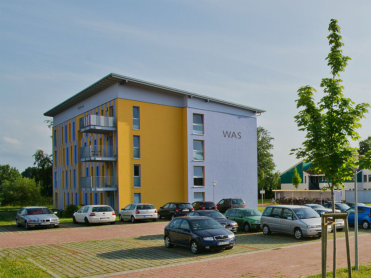Wohnheim Fleischerwiesen Modernes, rechteckiges Flachdachgebäude des Studentenwohnheim mit Parkplatz und Begrünung im Vordergrund.