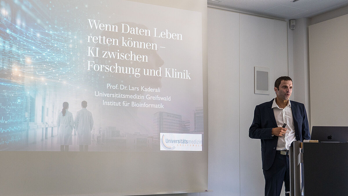 Ein Mann hält einen Vortrag vor einem großen Bildschirm mit Text zu KI und Forschung