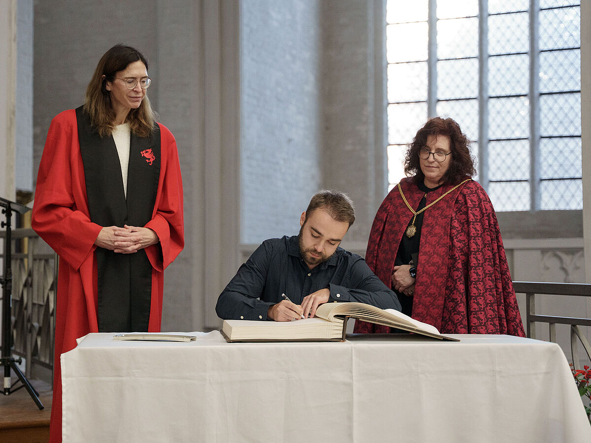 Symbolbild Immatrikulationsfeier Winter 2025/26: Ein Studierender schreibt sich in das Goldene Buch der Universität Greifswald ein.